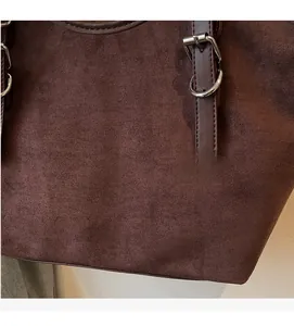 Dettaglio della trama in camoscio marrone con tracolla in pelle e fibbia in metallo