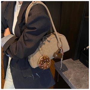Detail of khaki Boston bag featuring white stitching and a plush donut charm accessory