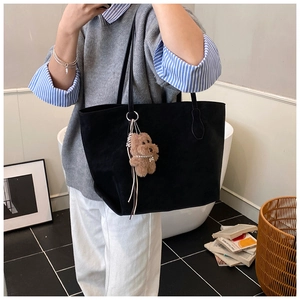 Black large tote bag with brown plush bear charm shown in a lifestyle street setting