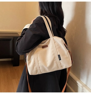 Detail of beige canvas tote bag with brown leather logo and adjustable shoulder strap