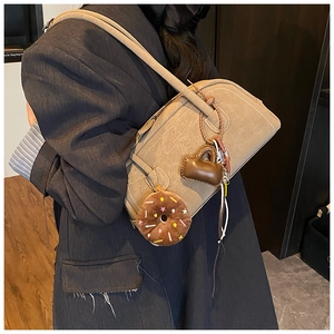 Detail of khaki Boston bag with cute donut charm and mini bag accessory on leather