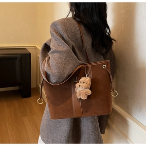 Detail of dark brown suede tote bag with metal ring and plush teddy bear charm