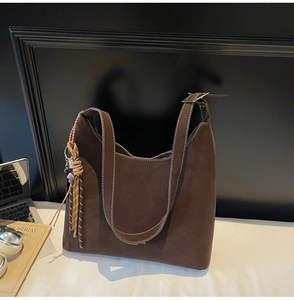 Detail of a large brown suede tote bag with fringe charm and metallic strap buckles