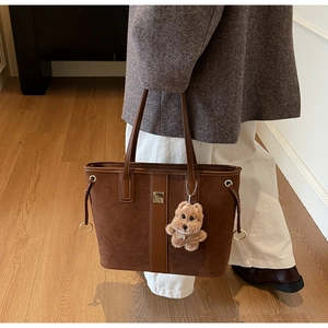 Detail of a brown suede tote bag featuring a cute plush dog pendant and metal buckle