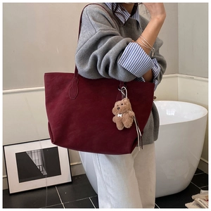 Detail of burgundy tote bag with soft suede texture and cute brown plush bear charm