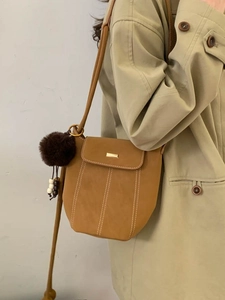 Retro tan bucket crossbody bag with plush charm and stitching on a khaki trench coat