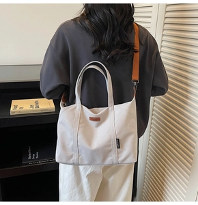 Detail of canvas tote with reinforced leather handles and wide orange shoulder strap