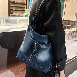 Detail of washed denim crossbody bag featuring metal zippers and multiple side pockets