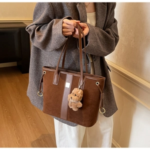 Detail of a large brown suede tote bag with leather trim and plush puppy charm