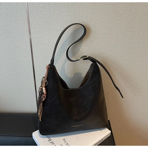 Detail of black leather bucket bag featuring a woven tassel charm and minimalist logo