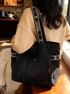 Minimalist large capacity black canvas tote bag with jacquard shoulder strap worn outdoors