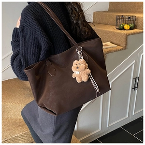 Detail of dark brown tote bag with suede texture and cute plush bear charm on the handle