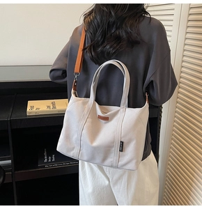 Detail of white canvas tote with brown straps and leather logo for daily commute