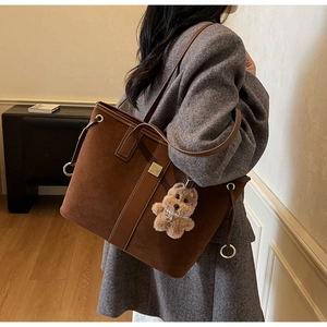 Detail of dark brown suede tote bag featuring side metal rings and plush bear charm