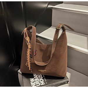 Detail of dark brown tote bag with fringe charm and heart embroidery on artsy book