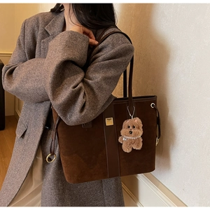 Detail of coffee brown suede tote bag featuring a cute teddy bear charm accessory