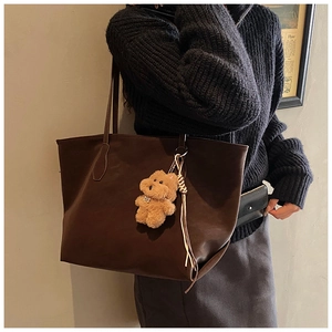 Detailed side view of large brown faux leather tote bag with a plush bear charm accessory