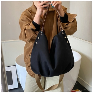 Detail of black canvas tote bag with brown leather handle and wide woven shoulder strap