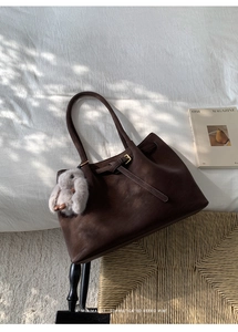 Detail of dark brown leather tote bag with matte finish and cute plush rabbit charm