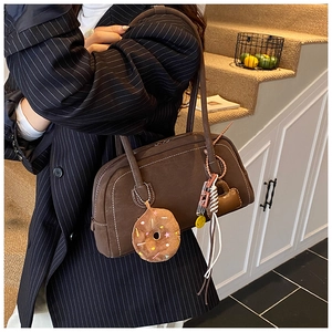 Detailed side view of vintage brown Boston bag with fuzzy donut charm and white stitching