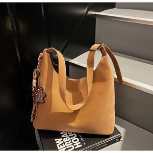 Detail of khaki leather bucket bag featuring leopard bear charm on a lifestyle background