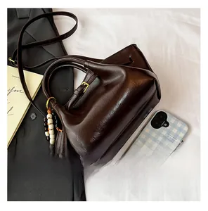 Detail showing deep brown leather handbag with gold hardware and beaded charm on white fabric