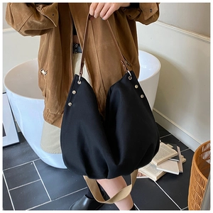 Detail of black canvas tote bag with brown leather handles and silver studs shown on floor