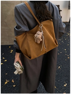 Detail of high-capacity camel leather tote bag with teddy bear charm and ribbon strap
