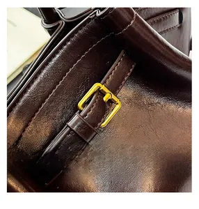 Detail of dark brown oil wax leather handbag showing fine stitching and gold buckle