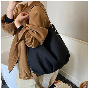 Detail of black canvas tote bag showing wide brown strap and high-quality fabric texture