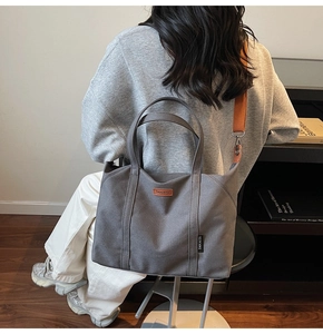 Detail of grey canvas tote bag featuring brown leather logo and orange shoulder strap