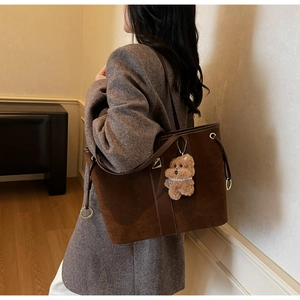 Detail of dark brown suede tote bag with plush puppy pendant and metal ring buckle