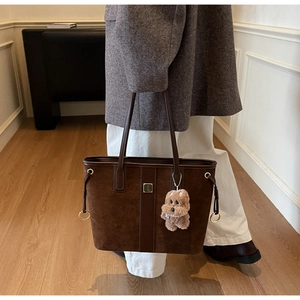 Close-up of a brown suede tote bag featuring a cute plush dog charm and gold hardware