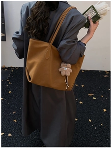 Caramel brown large tote bag with plush bear charm on a dark grey wool coat background