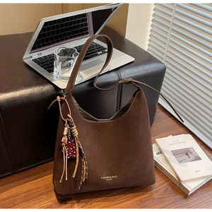 Detail of dark brown leather hobo bag with tassel and laptop in a workspace