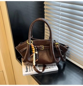 Detail of dark brown faux leather tote bag with wing shape and wooden bead tassel