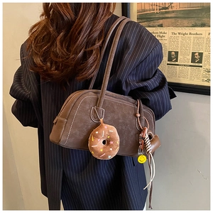 Detail of vintage brown suede shoulder bag with white stitching and plush donut charm