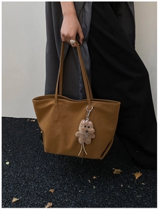 Close-up of caramel brown leather tote bag with a cute plush dog pendant accessory