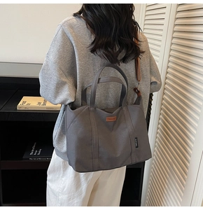 Deep grey canvas tote bag with adjustable brown strap shown in a casual lifestyle setting