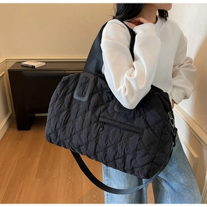 Detail of black quilted sports tote bag with fine floral embroidery and metal buckle