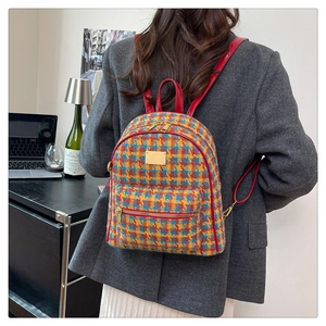 Détail d'un sac à dos en tweed à carreaux avec bretelles rouges et zips dorés