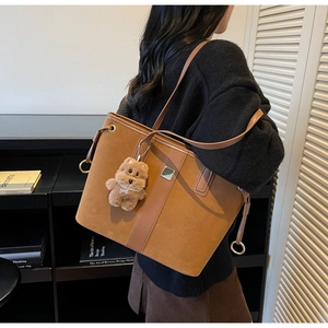 Close-up of brown suede tote bag featuring leather straps and a cute plush bear charm