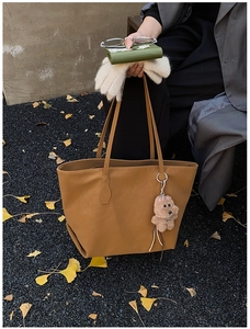 Brown leather tote bag with bear charm shown on autumn leaves background