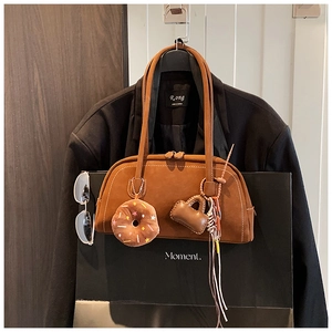 Close-up of brown suede Boston bag with plush donut charm and decorative long tassels