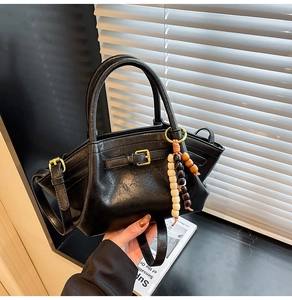 Detail of black trapezoid handbag with metallic side buckles and colorful wooden bead charm