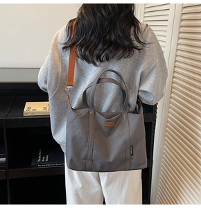 Deep gray canvas tote bag with contrast orange strap worn by a model in a cozy setting
