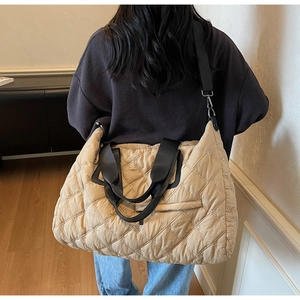 Detail of large quilted beige tote bag with black strap in a cozy interior setting