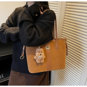 Detail of a large brown suede tote bag featuring a cute teddy bear charm and metal tag
