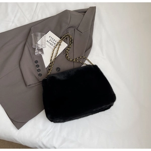 Détail d'un sac bandoulière noir en peluche avec une chaîne dorée sur tissu blanc