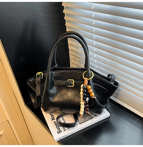 Detailed shot of a black pebbled leather handbag with wooden bead charm on a book